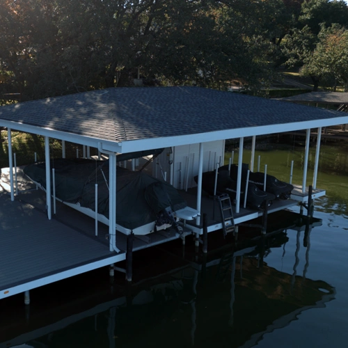 A modern lakeside dock on Lake Granbury featuring an offset design with a spacious covered area. The dock includes boat slips, jet ski lifts, and a storage room, all surrounded by a sleek, open deck for entertaining. Designed to maximize lake views while providing ample space for social gatherings.