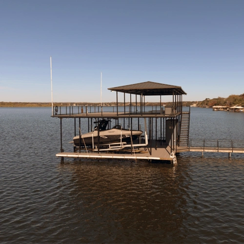 A modern two-story waterfront dock on Lake Granbury, designed for both recreation and fitness. The structure features a covered upper deck with open space for workouts and relaxation, while the lower deck includes a boat lift, swim ladder, and easy water access. The sleek black metal framework and composite decking blend seamlessly with the natural surroundings, creating the ultimate athletic retreat on the water.