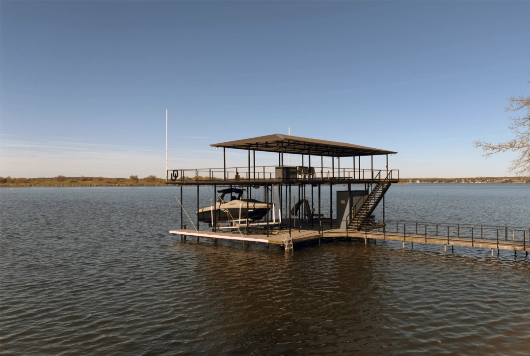 Aerial view of a two-level waterfront fitness retreat on Lake Granbury, featuring a spacious upper deck with shaded seating areas and an open lower deck equipped for boat storage, workouts, and lake access.