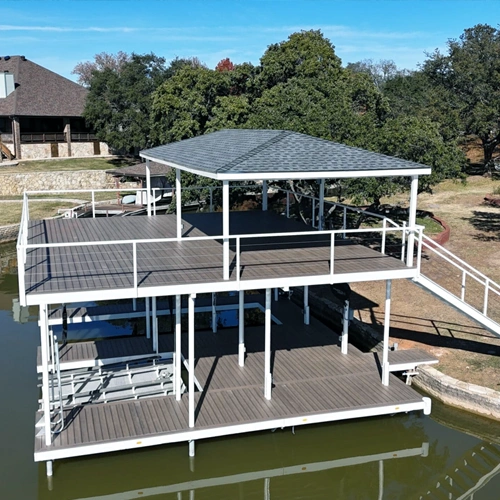 A beautifully designed two-story boat dock on Lake Granbury, featuring a spacious upper deck with a covered seating area and a lower level with boat slips and swim platforms. The dock's sleek white railing and composite decking create a modern, inviting space for family gatherings and waterfront enjoyment.