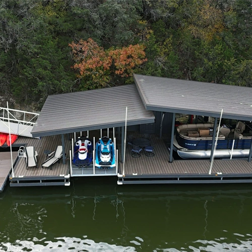 Aerial view of The Nemesis Project, a cutting-edge floating dock with a striking split, tilted roof system. The dock seamlessly blends with the rugged lakeside terrain, featuring dedicated boat and personal watercraft lifts, a spacious entertainment area, and a steel gangway for cliffside access. Designed to overcome extreme site challenges, this modern structure embodies architectural innovation and premium waterfront functionality.