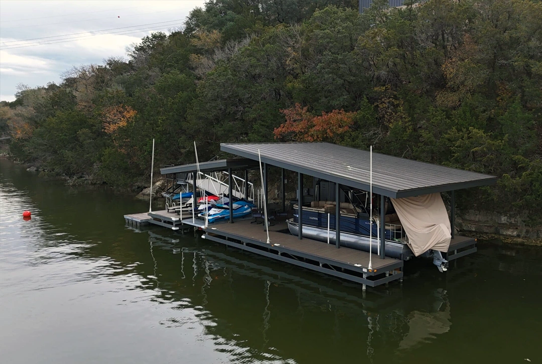 A side angle of the Nemesis dock, showing a large covered slip sheltering a luxurious pontoon boat. The tilted rooflines add a dynamic architectural element, while the sturdy pilings and dock framework demonstrate the durability of the structure.