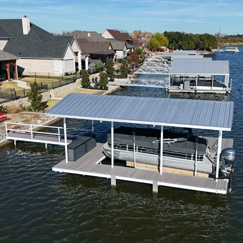 Aerial view of the completed Paquin Project, a stationary dock designed to comply with HOA guidelines while preserving waterfront aesthetics. The dock seamlessly integrates with the neighborhood's floating structures, featuring a sleek metal roof, spacious decking, and a covered boat lift on Lake Granbury.